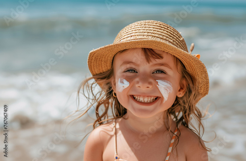 A nice little girl in a straw hat, smiling with her face smeared with sunscreen on the beach. Children, sun protection and beach concept.