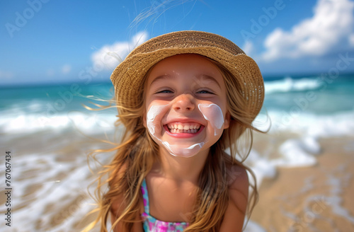 A nice little girl in a straw hat, smiling with her face smeared with sunscreen on the beach. Children, sun protection and beach concept.
