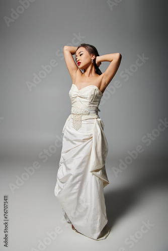 pretty asian woman in white dress with red lips putting hand behind head and looking to down