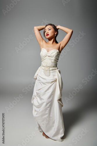 attractive asian young woman in white dress with red lips putting hand behind head and looking to up