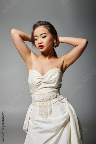 beautiful asian woman in bridal outfit with red lips putting hand behind head and looking to down