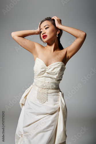 pretty asian woman with red lips holding to head and looking to down on grey background