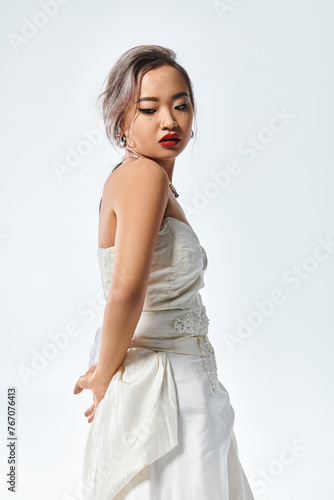 charming asian young woman with red lipstick and pearl necklace looking behind back