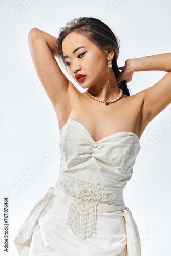 alluring asian young woman in bridal outfit looking to down and putting hands behind head