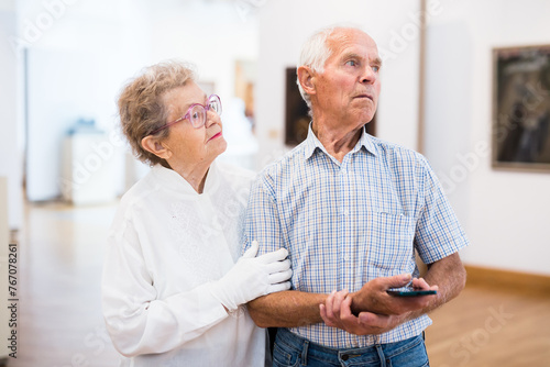 Mature European couple examines paintings in an exhibition in hall of art museum photo