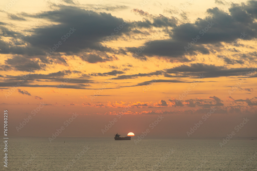 Sun setting over the ocean with a large ship slightly in front of the setting sun. 