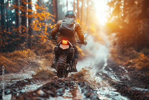 back of male motorcyclist on a sport enduro motorcycle races on dirty forest road at sunset in summer photo