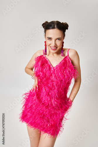 Fabulous brunette woman in trendy pink dress and fancy jewelry laughing joyfully isolated on grey photo