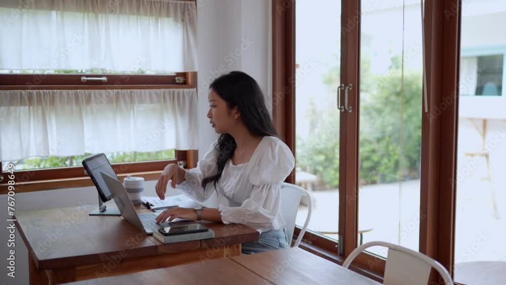 An Asian young businesswoman is working at a nearby café, using her laptop with focus and determination An Asian young businesswoman is working at a nearby café, using her laptop with focus and determination