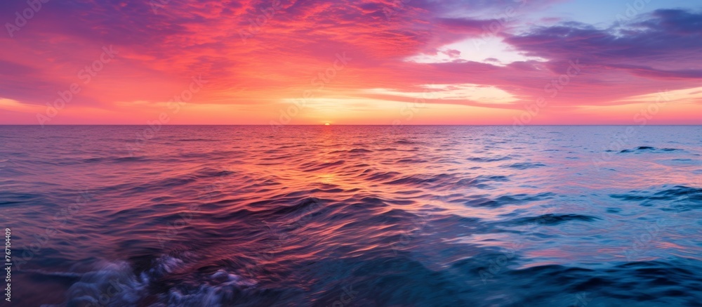 As dusk falls, the sunset paints the sky over the ocean in shades of purple, creating a stunning natural landscape. Clouds reflect in the water, adding to the serene atmosphere of the afterglow