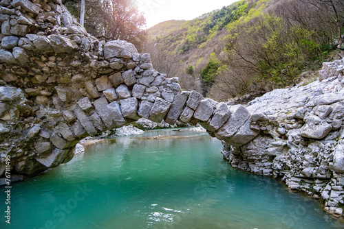 Beautiful stone semi-arch bridge over a river with blue water in the mountains