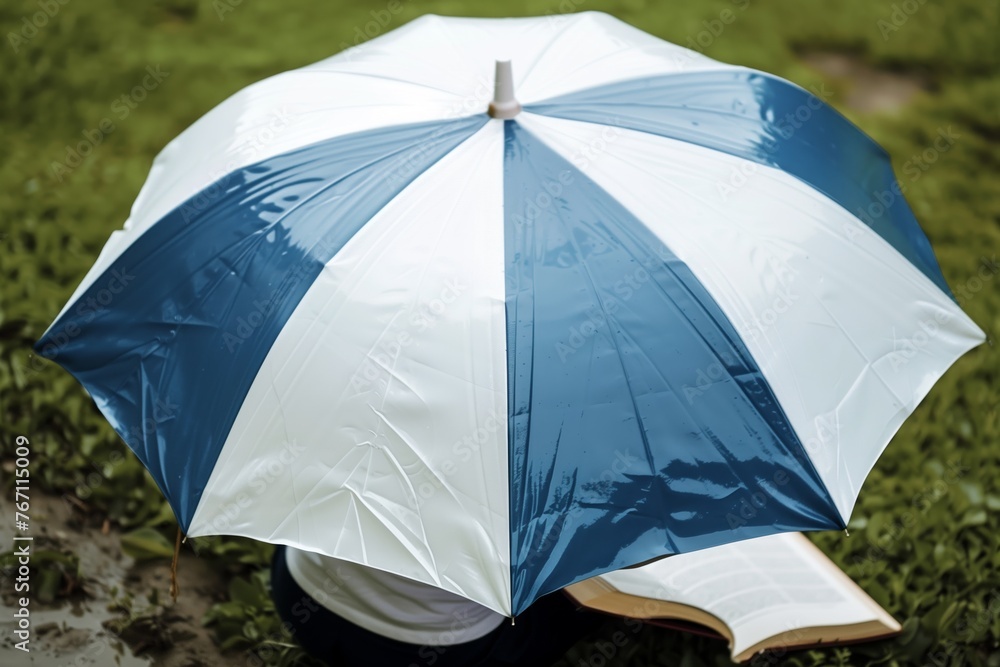 white and blue umbrella with a person reading a book underneath