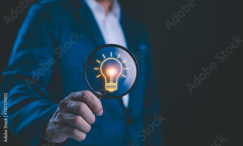 Businessman holding a magnifying glass that illuminates a light bulb icon, representing insight, innovation, and the search for bright ideas in the corporate world. Business solution idea concept.