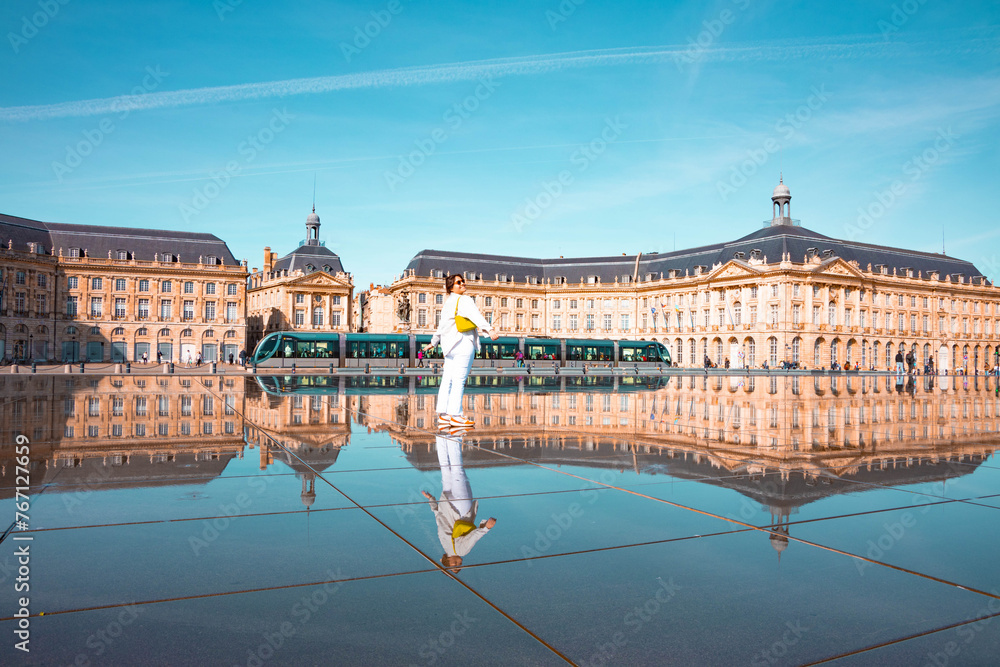 Happy latin woman walking on the Bordeaux town square with palace and mirror of water.