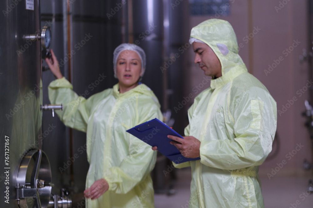 Winemaker woman and business owner wearing a sterile suit working and inspecting wine tanks in a large winery factory liquor drink industry quality and fermentation monitor in a wine factory