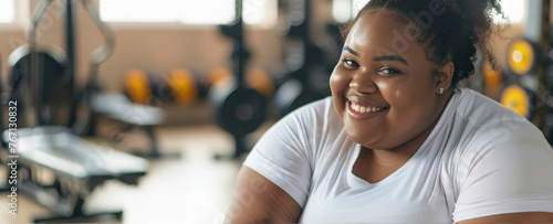 A positive smiling young Asian woman in a white sports T-shirt against the background of a sports gym. The concept of body positivity. The concept of fighting excess weight. © Olga