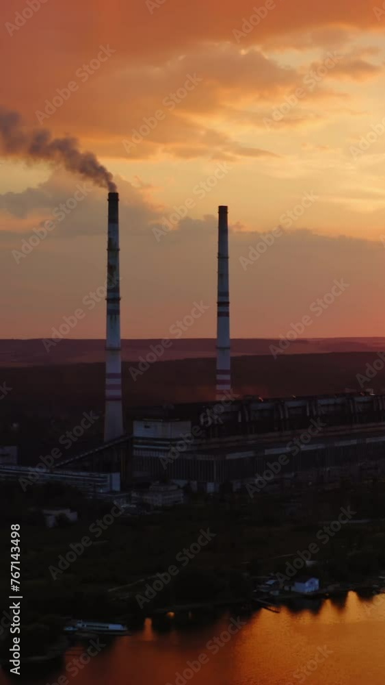 Factory near the river at sunset. Industrial plant with smoking pipe against the evening sky. Ecological problems. Motion camera back. Aerial view. Vertical video Factory near the river at sunset. Industrial plant with smoking pipe against the evening sky. Ecological problems. Motion camera back. Aerial view. Vertical video