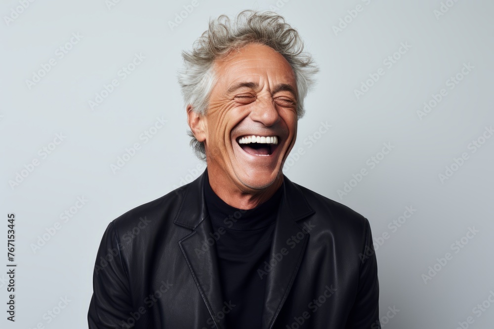 Handsome mature man laughing and looking at camera while standing against grey background