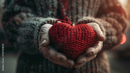 Close-up senior old hands hold knitted heart in hands in winter street. Share love with those who ne