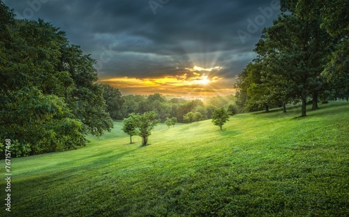 the sun sets over a green field with trees on either side