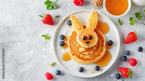 Easter breakfast. Children's scene featuring a pancake shaped like a cute bunny, surrounded by berries and honey on a light gray concrete background.