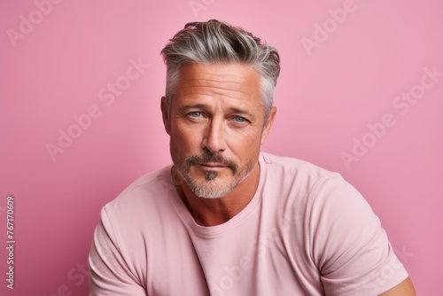 Portrait of handsome mature man with grey hair and beard looking at camera while standing against pink background