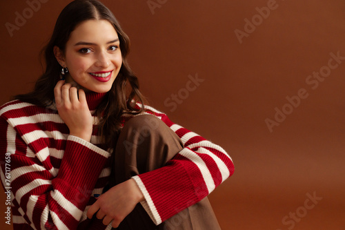 Fashionable happy smiling beautiful woman wearing red striped knitted turtleneck sweater,  posing on brown background. Close up studio fashion portrait. Copy, empty, blank space for text