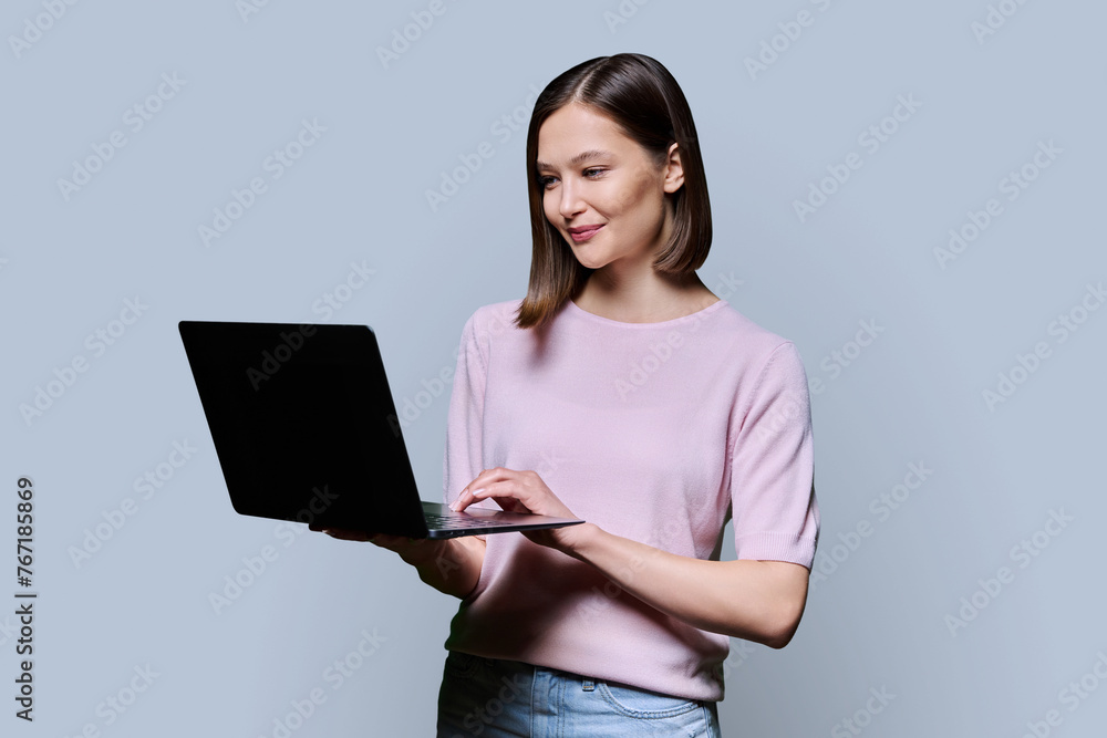 Smiling young woman with laptop on grey studio background Smiling young woman with laptop on grey studio background