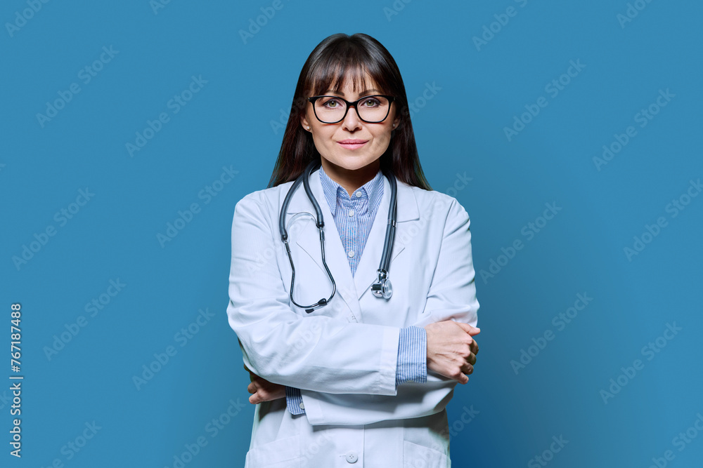 Confident friendly female doctor with crossed arms on blue background Confident friendly female doctor with crossed arms on blue background