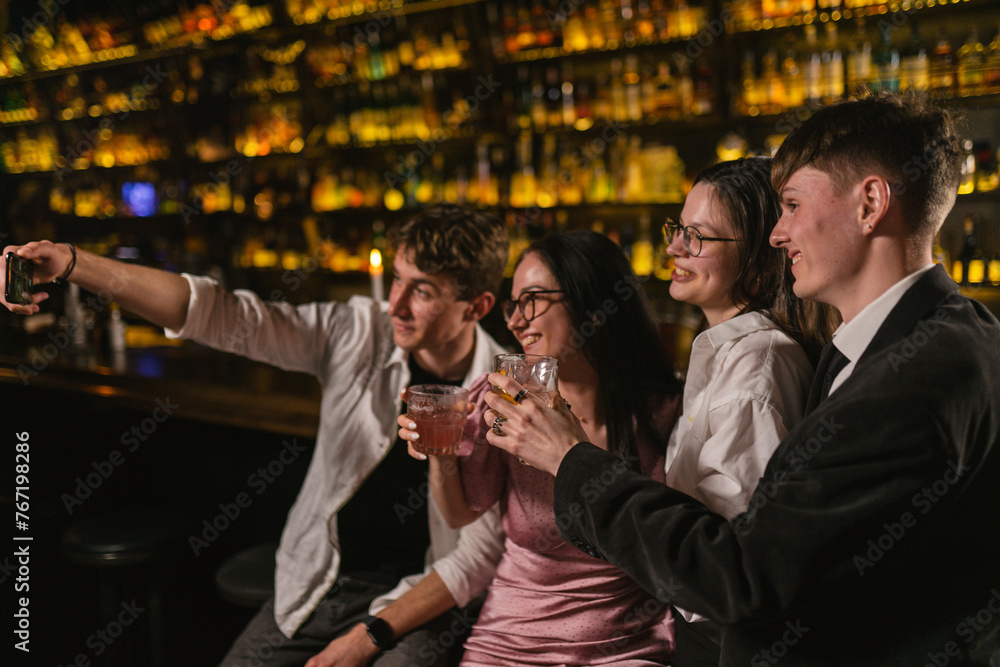 Friends rejoice at meeting with delicious cocktails in cozy pub. Young guy photography with close friends after funny party at bar