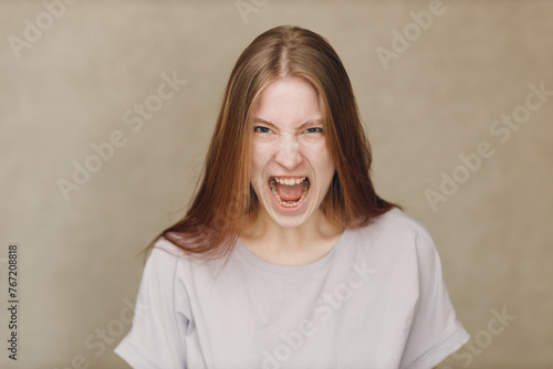 Portrait of shout screaming young caucasian woman looking at camera against beige background. Casting film movie acting auditions.