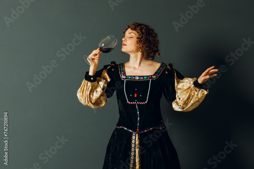 Young adult woman dressed in a medieval dress holding a glass of wine and drinking a red wine