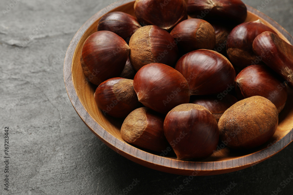 Roasted edible sweet chestnuts in bowl on grey textured table, closeup Roasted edible sweet chestnuts in bowl on grey textured table, closeup