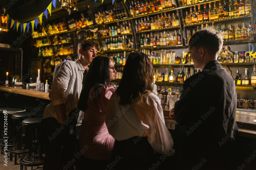 Guys and girls drink cocktails in bar with patriotic symbols. Girls and men tired after party and company continues talking at bar counter
