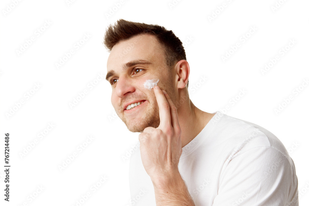 Young handsome man applying facial care, day cream and looking away against white studio background. Concept of natural beauty, spa treatments, masculine, cosmetology. Young handsome man applying facial care, day cream and looking away against white studio background. Concept of natural beauty, spa treatments, masculine, cosmetology.