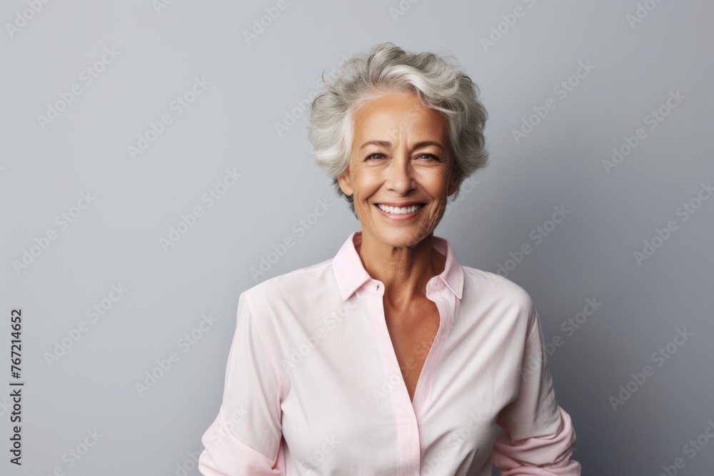 Mature woman with grey hair. Portrait of beautiful senior woman smiling at camera while standing against grey background Mature woman with grey hair. Portrait of beautiful senior woman smiling at camera while standing against grey background