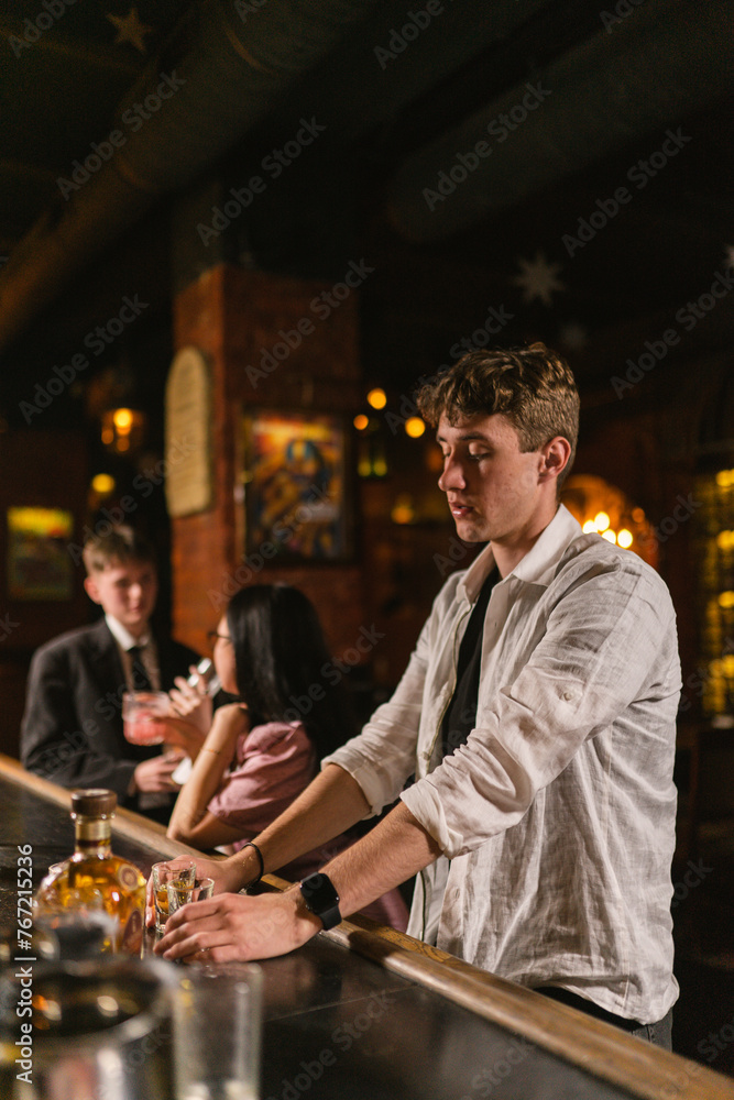 Guy in white shirt with bottle of whiskey sits in cozy pub. Man sits alone after fun holiday and listens loud music in night pub
