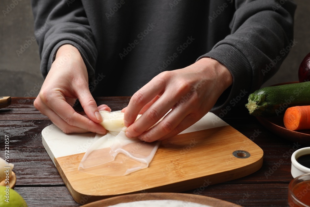 Making delicious spring rolls. Woman wrapping fresh cabbage into rice paper at wooden table, closeup Making delicious spring rolls. Woman wrapping fresh cabbage into rice paper at wooden table, closeup