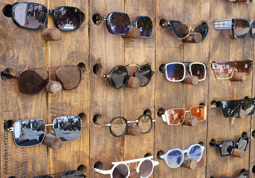 Varied Sunglasses Displayed on Wooden Stand. A collection of different sunglasses displayed on a wooden board for sale at an outdoor market.
