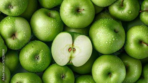 A cluster of green apples with water droplets, one cut in half revealing the seeds.