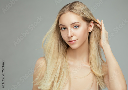 Beautiful Blondie Girl with Long Silk Hair showing Ear. Beauty Model with Natural Makeup and Blond Hairstyle over Gray background