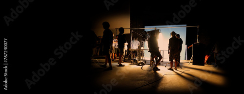 Silhouette images of video production behind the scenes of making of TV commercial movie shoot that film crew team lightman and camera man working together with director and equipment in big studio.