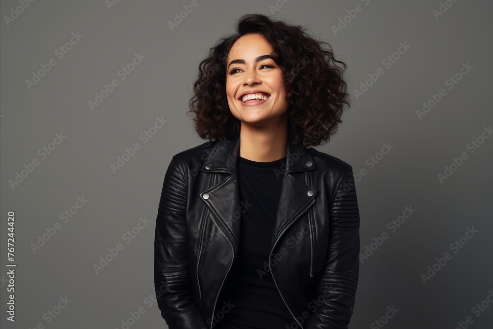 Portrait of a happy young woman in leather jacket posing against grey background Portrait of a happy young woman in leather jacket posing against grey background