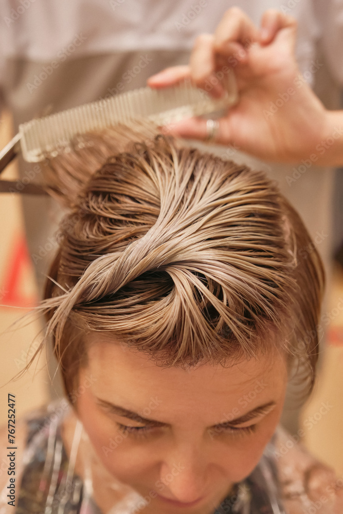 Naklejka premium Hairdresser trimming blond hair with scissors. Haircut closeup. Barber using scissors and comb. Creating hairstyles by a hairdresser in the salon. Shallow depth of field. Toned image