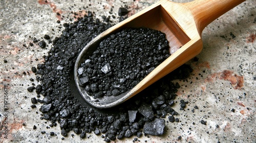 Wooden scoop with black Himalayan salt on a concrete surface. photo