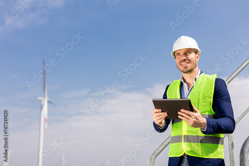 Smiling Engineer With Tablet Inspecting Wind Turbines On A Sunny Day