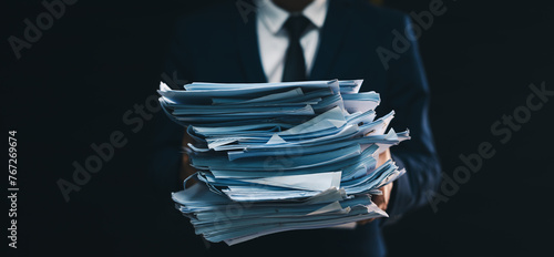 business man holding full of paper documents. Office l with stack binders for archiving documents over black isolated background.