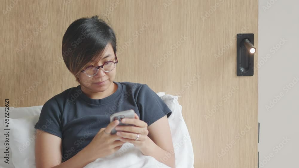 Close up face of pretty asian woman who is using smartphone for chatting and texting with morning sunlight in the wooden furnished bed shows concept of relaxation and comfort for weekend refreshing. Close up face of pretty asian woman who is using smartphone for chatting and texting with morning sunlight in the wooden furnished bed shows concept of relaxation and comfort for weekend refreshing.