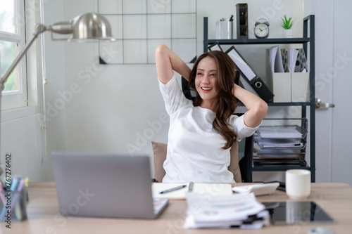 A young woman relaxes with her hands behind her head, taking a break in home office.