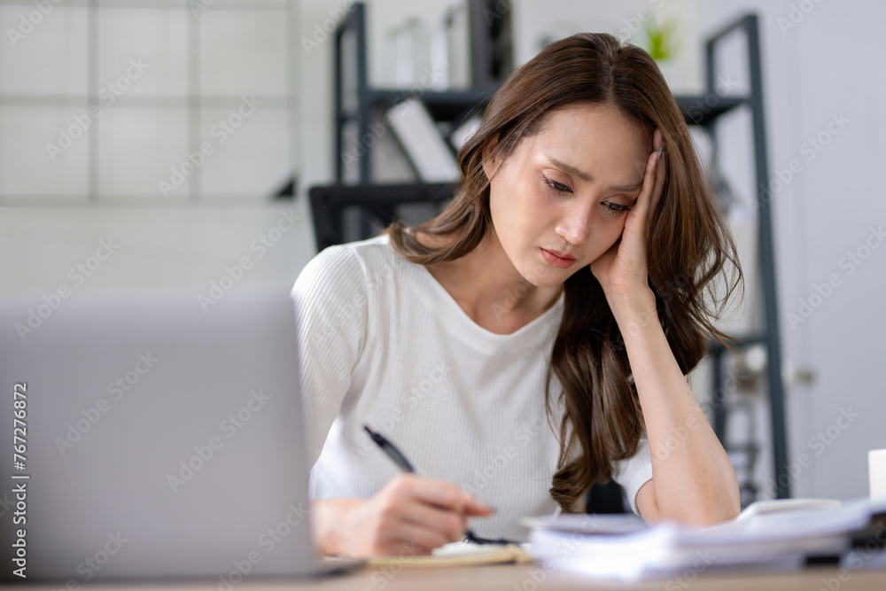 A businesswoman appears stressed and experiencing a headache while focusing on her work in home office. A businesswoman appears stressed and experiencing a headache while focusing on her work in home office.